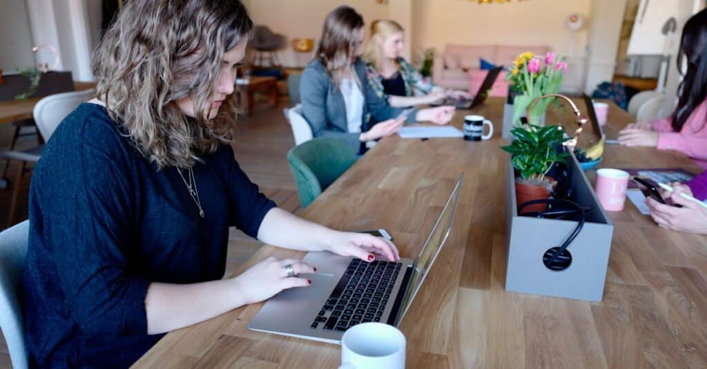 Group of women working in a modern coworking space with laptops and coffee.