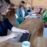 Group of women working in a modern coworking space with laptops and coffee.